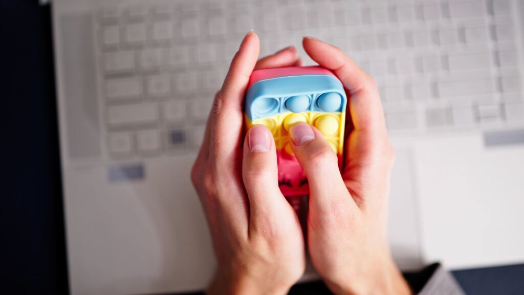 Techado de computadora de fondo con popit para la ansiedad y dos manos jugándolo